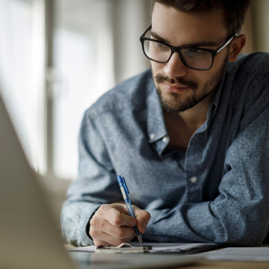 Smiling man in blue shirt seated at desk, representing Sukoon's DHA Essential Benefit Plan and customer-focused care