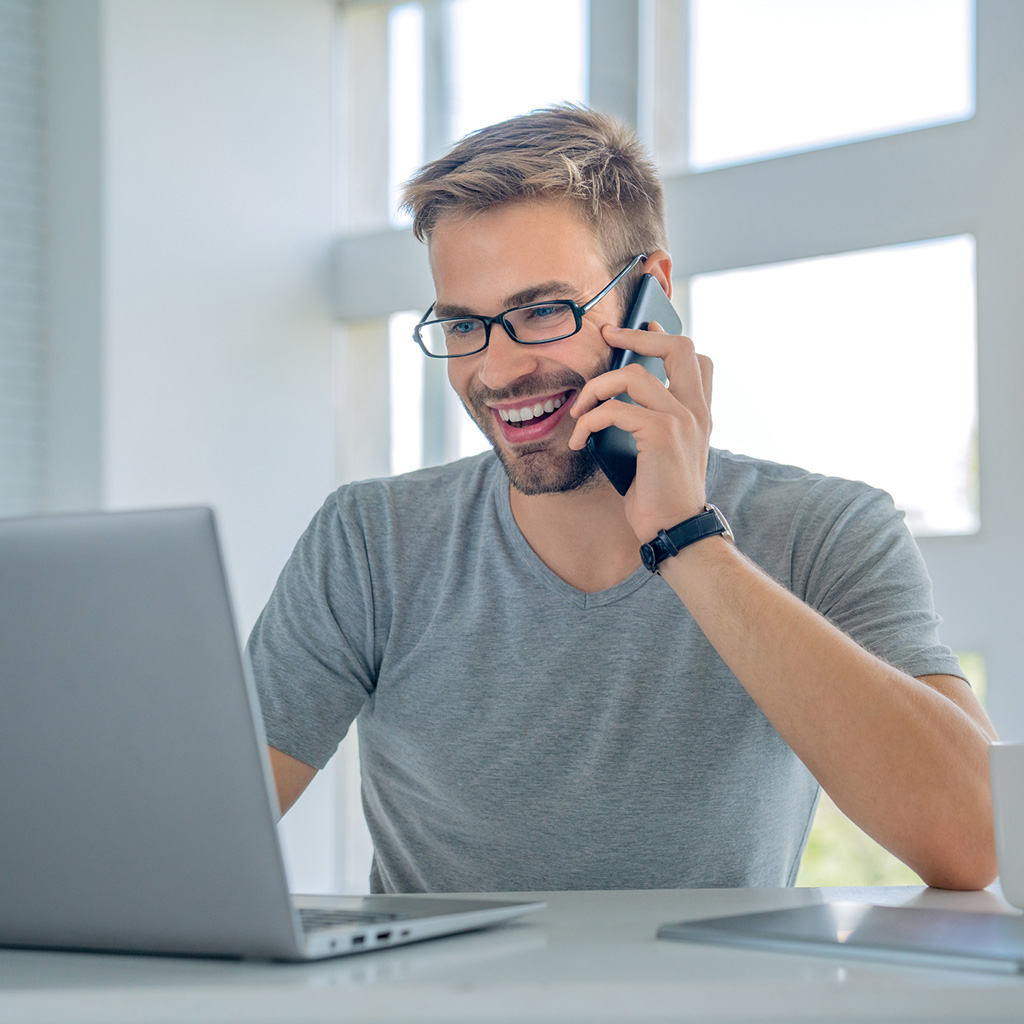 Smiling man on phone and laptop, representing peace of mind with secure health insurance from Health Extend
