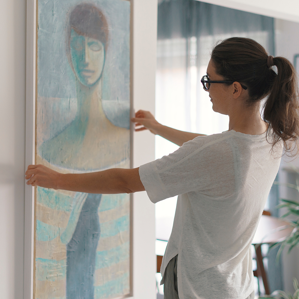 Privilege Home art insurance plan in Dubai, UAE. Covering luxury homes, art, jewelry & more. Brunette Woman hanging painting.